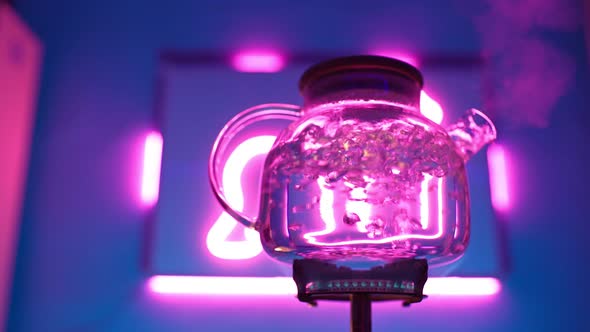 Transparent Kettle Boils on Gas Burner Against Neon Purple Backlight