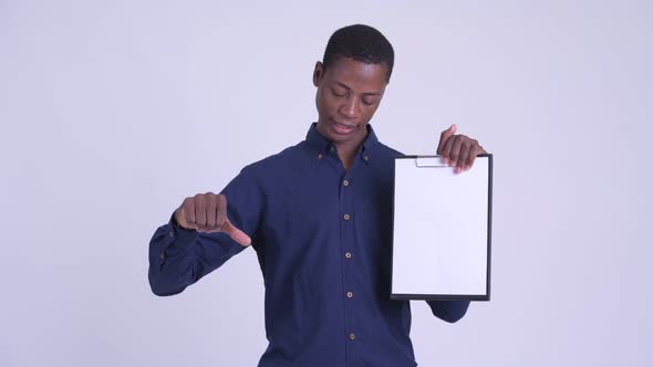 Young Stressed African Businessman Giving Thumbs Down While Showing Clipboard