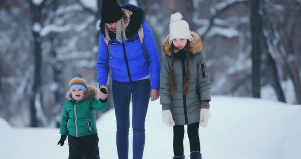 Mom and Son By the Handle and Daughter Go Through the Park in Winter