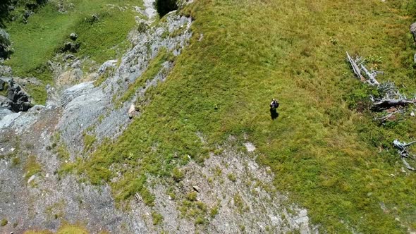 revealing aerial shot of a woman hiking on the edge of a mountain with a beautiful blue lake in the