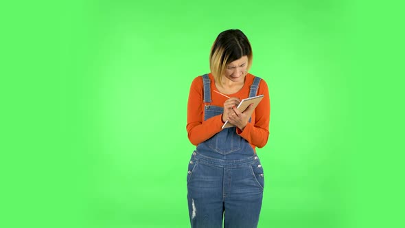 Girl Stands and Thinks, Then Intently Writes with Pencil in Notebook. Green Screen