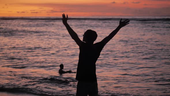 Silhouette of Man Raises His Hands Up Standing Back on Beautiful Tropical Beach on Red Sunset