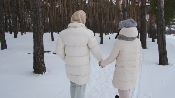 Two People Walk Hand in Hand in the Winter Forest