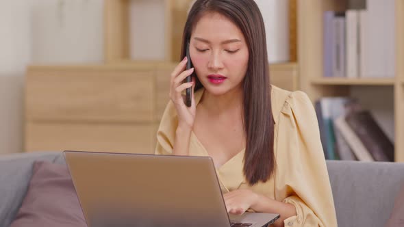 Beautiful Attractive Asian woman working on laptop smile and talking with customer in smartphone to