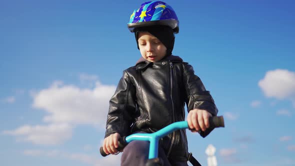 Baby Boy is Sitting on Children Bike in Protective Helmet on Country Road and Looks Into Distance