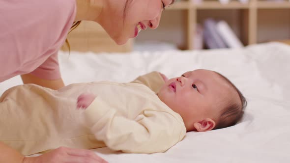 New asian mom playing to adorable newborn baby on bed smiling and happiness at home