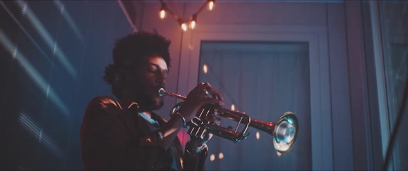 A young man listening to music with headphones and playing the trumpet with red neon light