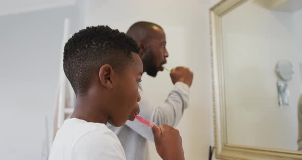 African american dad and son brushing teeth together looking in the mirror at home