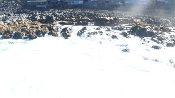 Aerial dolly tilt up slowly close to lava toward old fishing village