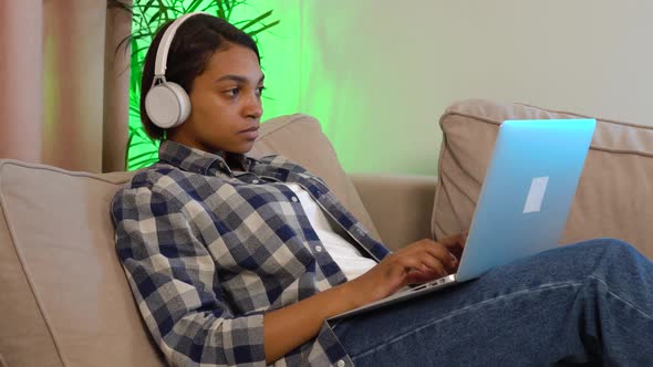 A Woman in a Casual Shirt with Headphones Holding and Using a Silver Laptop