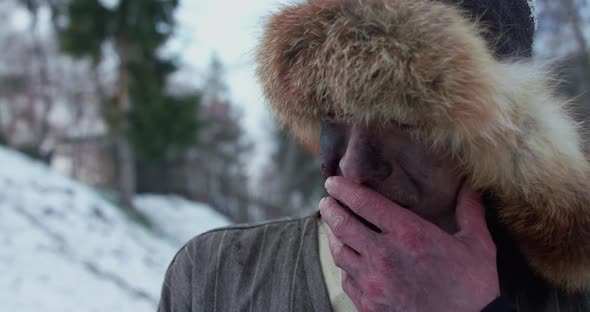 Exhausted Wounded Man in Fur Hat All in Blood Wipes Himself and Looks Up