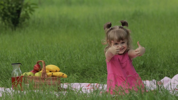 Weekend at Picnic. Lovely Caucasian Child Girl on Green Grass Meadow Sit on Blanket Waving Her Hands