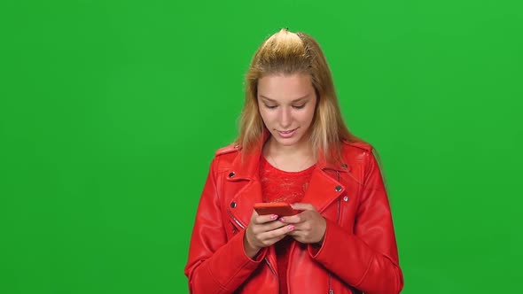 Portrait Blonde Girl Is Calmly Walking and Reading Text Message on Mobile Phone at Greenscreen