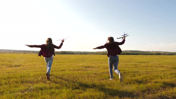 Toy Airplane in the Hands of Girls They Play on Field. Happy Kids in a Meadow with an Airplane in