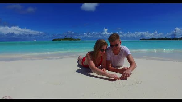 Boy and girl engaged on luxury shore beach lifestyle by aqua blue water and bright sandy background 