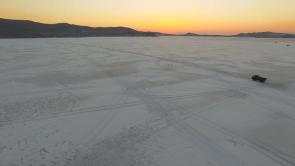 Drone View of a Small Truck Driving Across the Frozen Sea at Sunset