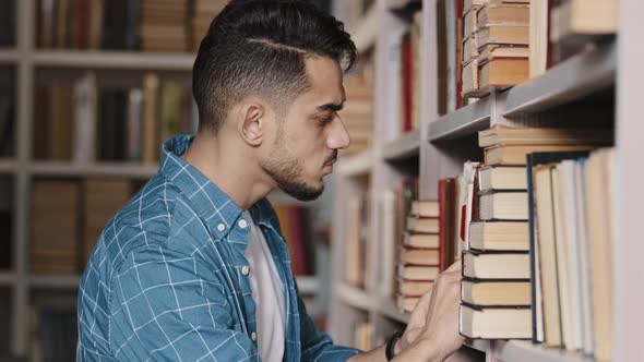 Closeup Serious Handsome Young Man Indoors Looking Attentively for Suitable Book on Bookshelf in