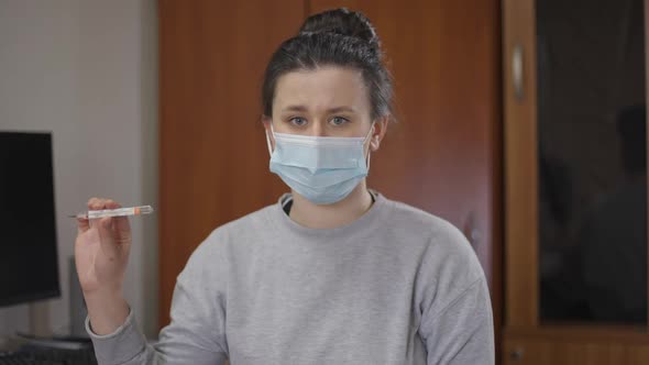 Young Upset Caucasian Woman in Covid Face Mask Showing Thermometer Touching Forehead Sighing Looking