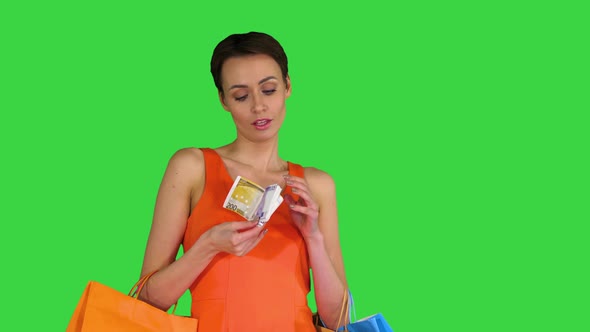 Beautiful Woman Holding Shopping Bags and Throwing Out Money Banknotes on a Green Screen, Chroma Key