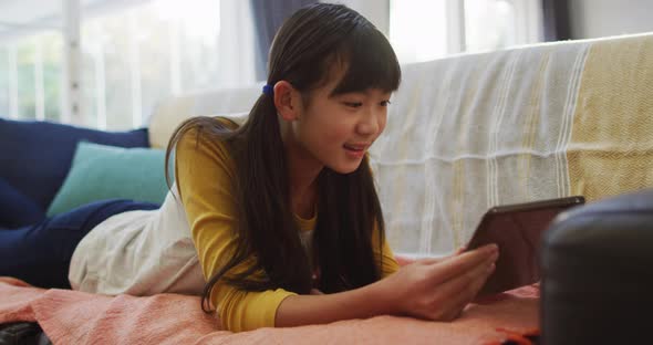 Asian girl smiling and using tablet lying on sofa at home