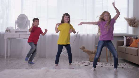 Dancing Kids in Multi Colored T-shirts Have Fun on Backround of Bright Window in a White Room During