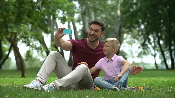 Father and Son Talking With Mother via Smartphone, Video Conference Outdoors
