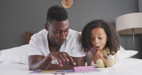 African american father reading a story to his daughter in bed