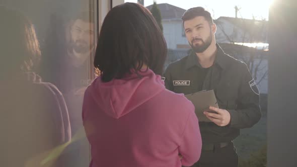 Portrait of Young Caucasian Police Officer Standing Behind Glass Door with Tablet and Talking