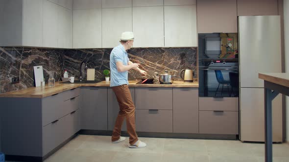 Man in a Hat Having Fun in the Kitchen While Cooking Dancing and Singing with a Ladle in His Hand