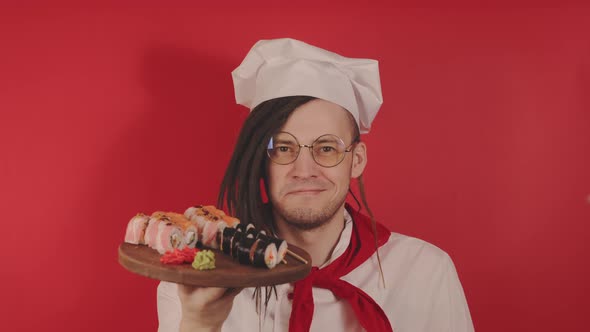 Young Man in Glasses Dressed As Chef Holding Wooden Board with Sushi Rolls