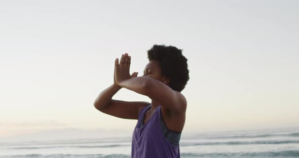 African american woman practicing yoga and meditating on sunny beach