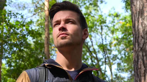 A Young Handsome Backpacker Stands in the Middle of a Forest and Looks Around - Face Closeup