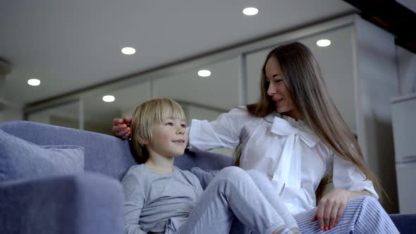 Excited Young Caucasian Mother and Cute Little Son Sitting on Couch Watching TV Talking and Pointing