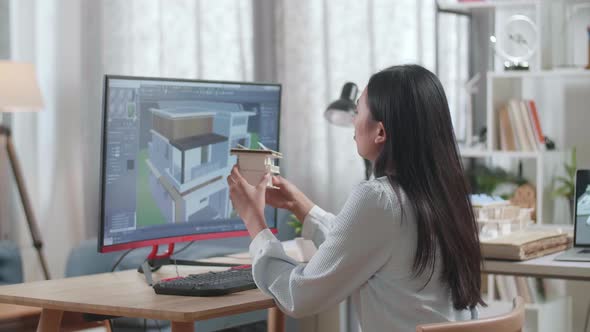 Asian Woman Engineer Holding And Looking At House Model While Designing House On A Desktop At Home