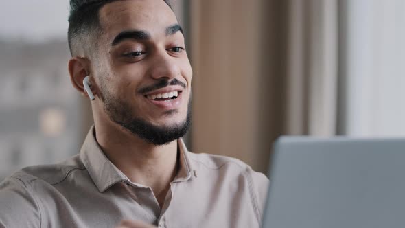 Smiling Hispanic Man Arab Guy Wears Wireless Earphones Using Electronic Device Talks at Computer Web