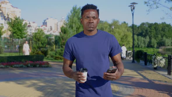 Afroamerican Man Uses Mobile Phone Holding White Cup with Coffee or Tea in Hand