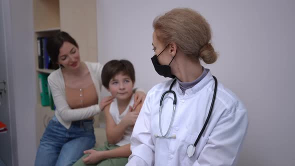 Confident Positive Doctor in Coronavirus Face Mask Looking Back at Happy Mother and Son Turning to