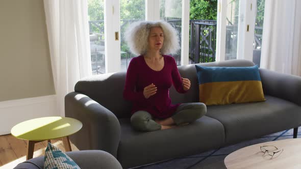 Senior caucasian woman practicing yoga while sitting on the couch at home