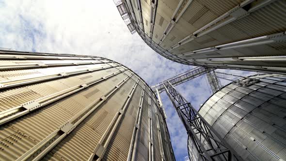 Grain elevators under blue sky. Huge metal grain storage tanks.