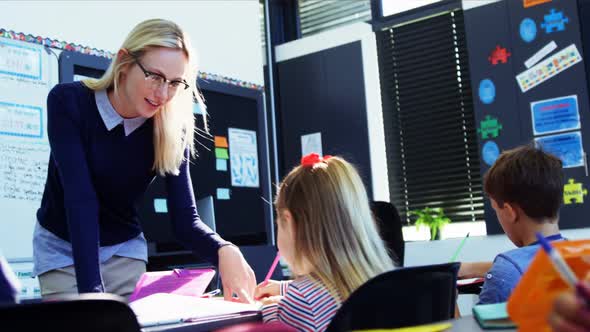 Teacher helping schoolgirl with her homework in classroom