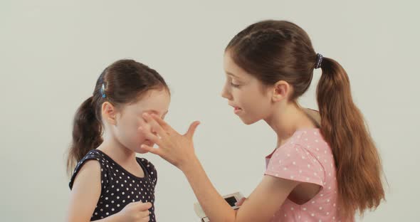 Girl helping her little sister to put on makeup in a white studio background