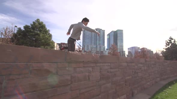 A young man freerunner doing parkour and flips over stone wall.