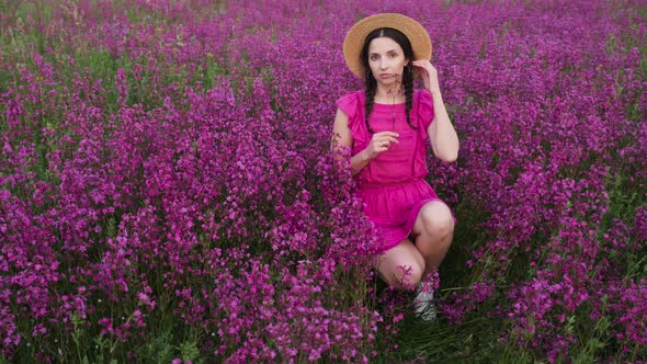 Girl in a Straw Hat and a Short Dress Sits in a Field