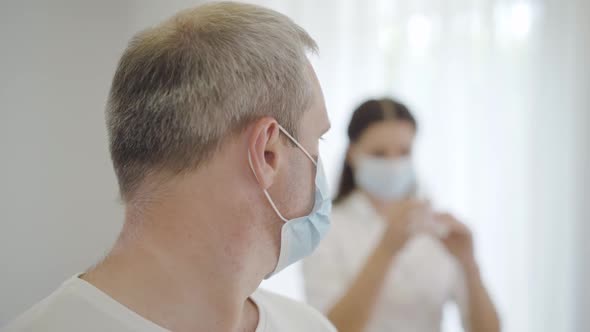 Close-up of Scared Male Patient in Face Mask Looking Back at Nurse Filling Syringe and Turning 