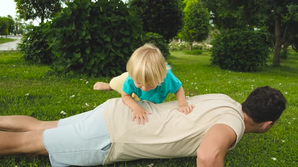 Child Climbs on the Father's Back While Father Does Pushups From the Floor in the Park