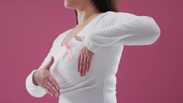 Mid section of a woman showing the pink ribbon on her chest against pink background