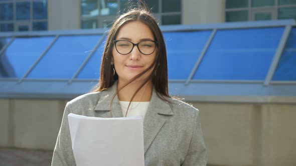 Young Woman in Suit and Glasses with Papers Smiling on the Street