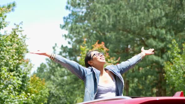 Cheerful woman spread arms on car rooftop under bright sky at mountain.