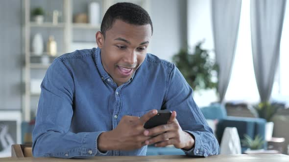 Young African Man Excited for Success While Using Smartphone