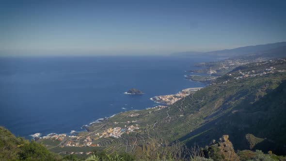 Scenic green hillside slopes toward azure sea far below and small coastal town of Tenerife, Canary I